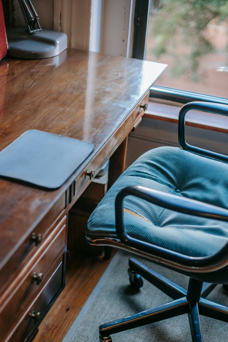 From above of domestic workplace in retro style with graphic tablet pad placed on old fashioned wooden table with drawers and soft armchair